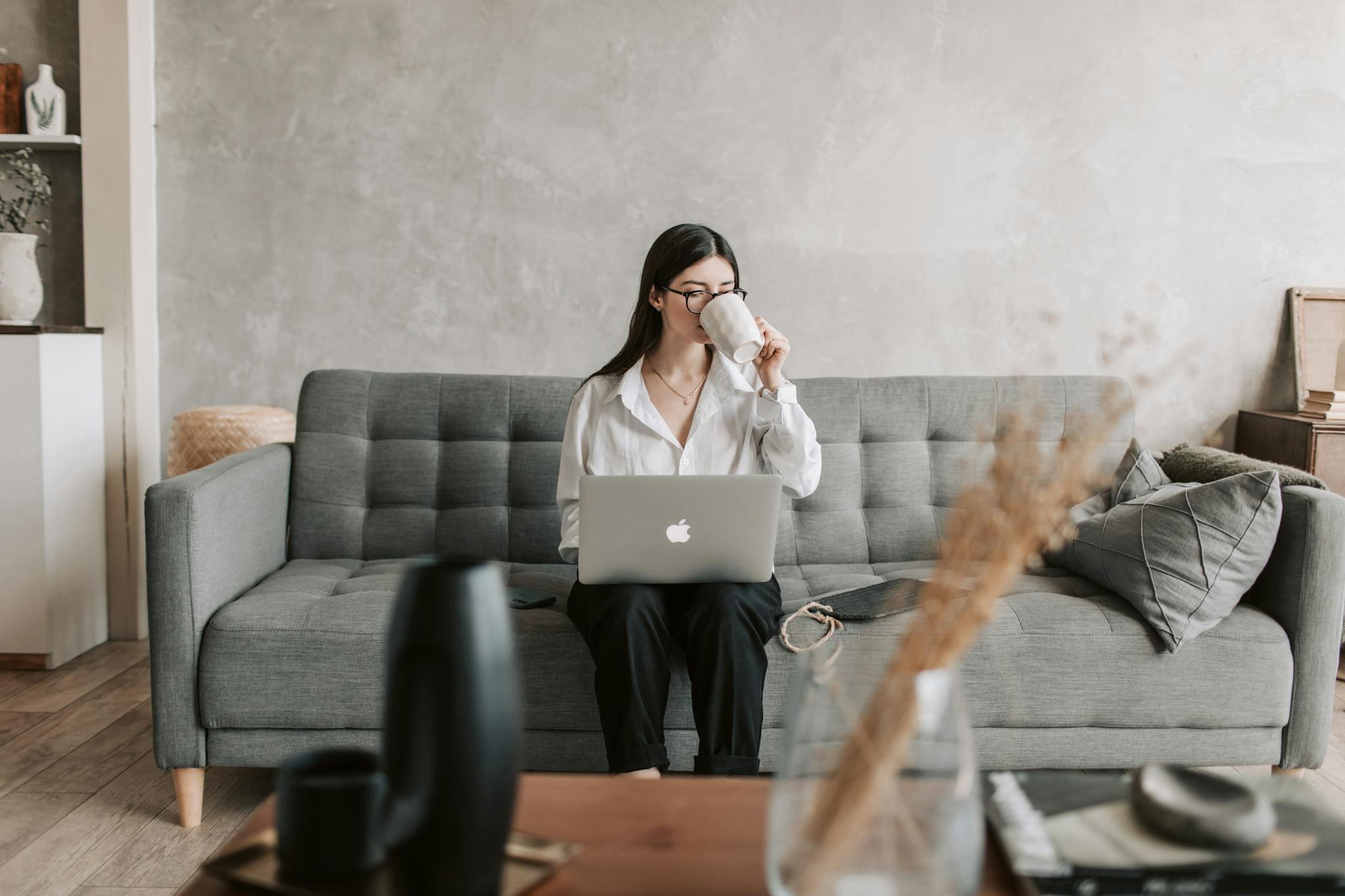 Woman sipping coffee while working on a laptop in a cozy home setting, highlighting remote work lifestyle.